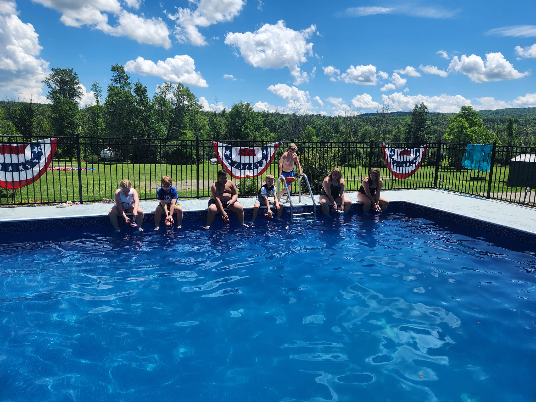 Campers lined up beside the pool under a bright blue sky
